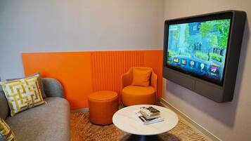 Una sala de estar moderna con un sofá gris, un reposapiés naranja y un televisor de pantalla plana montado en la pared.