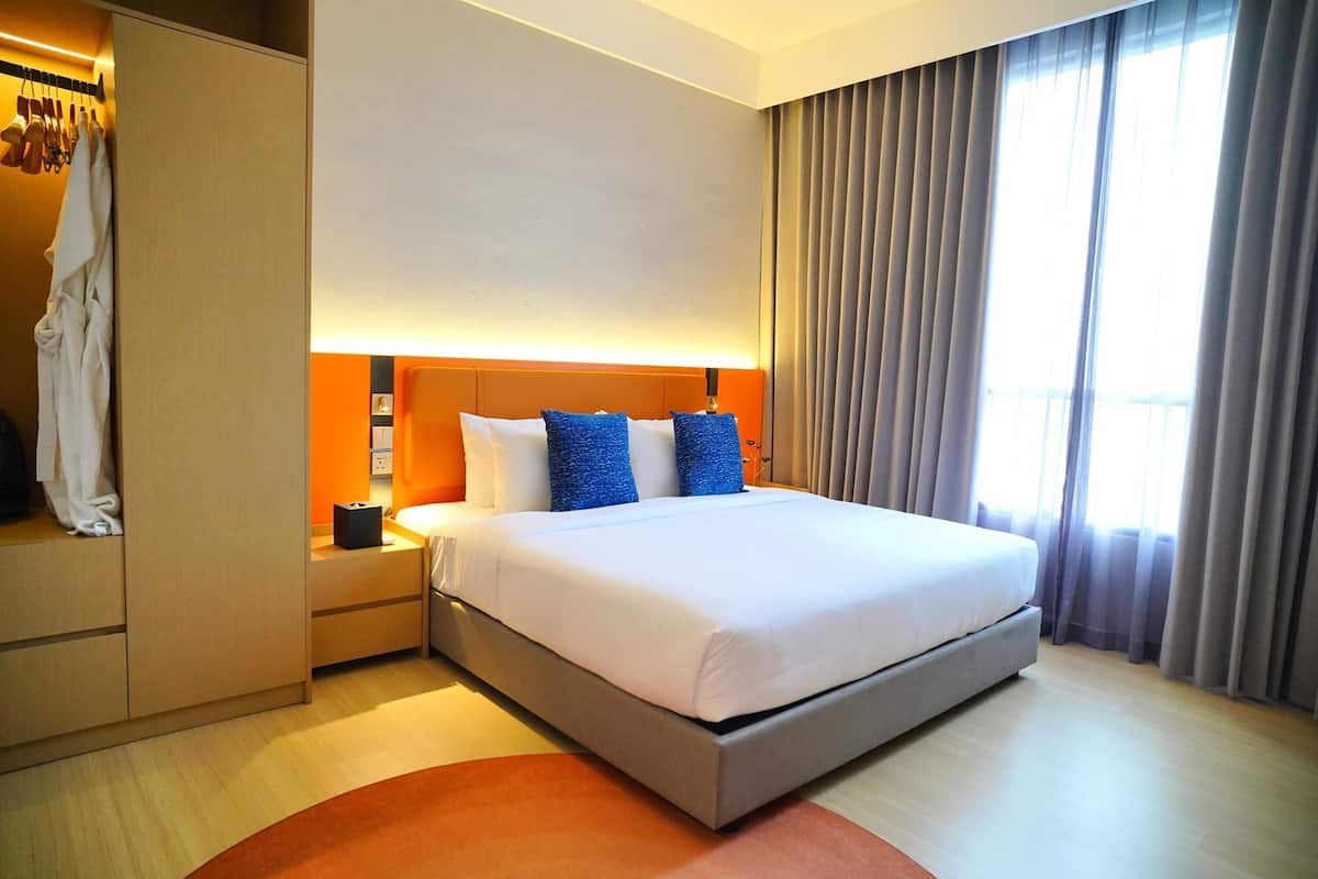 Une chambre d’hôtel avec un grand lit, une table de chevet, une armoire et une fenêtre avec des rideaux.