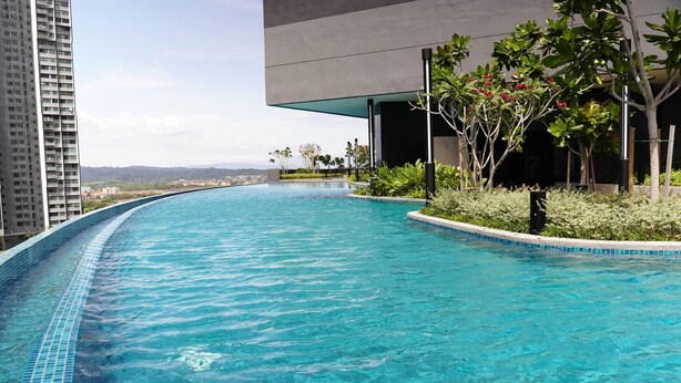 A modern swimming pool with clear blue water, surrounded by greenery and a view of distant buildings.
