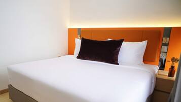 A neatly made bed with white linens and a dark brown pillow, a bedside table with a vase, and a wall-mounted light fixture.