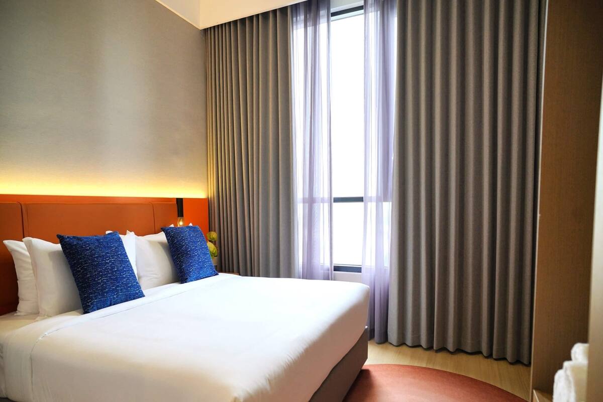 Une chambre d’hôtel avec un grand lit, une tête de lit et une fenêtre avec des rideaux.