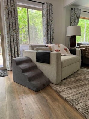 A living room with a sofa, a lamp, a staircase, and a view of greenery outside. - 100-Acre Luxury, Dog-Friendly, Sleeps 8-10 (Denver Township)