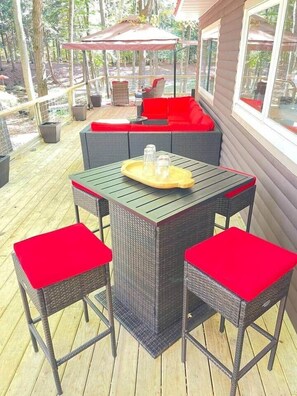A covered outdoor patio with a table and chairs, a red umbrella, and a seating area with cushions. - 100-Acre Luxury, Dog-Friendly, Sleeps 8-10 (Denver Township)