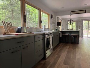 Une cuisine moderne dotée d’un îlot central, de planchers en bois et de grandes fenêtres.