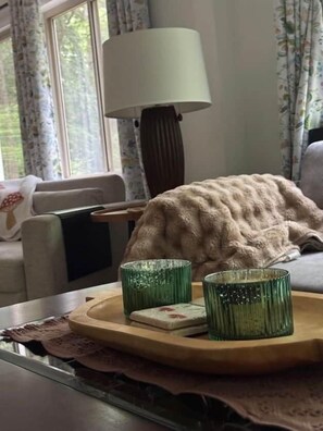 Une pièce confortable avec une fenêtre, une lampe, un canapé et un plateau avec des verres.