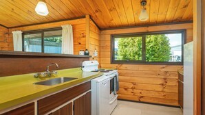 Une cuisine compacte aux murs en bois, dotée d’un plan de travail jaune, d’un évier, d’une cuisinière et d’une fenêtre donnant sur un paysage verdoyant.