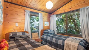 Une cabane avec deux lits, des murs en bois, une lampe suspendue et de grandes fenêtres avec des rideaux.
