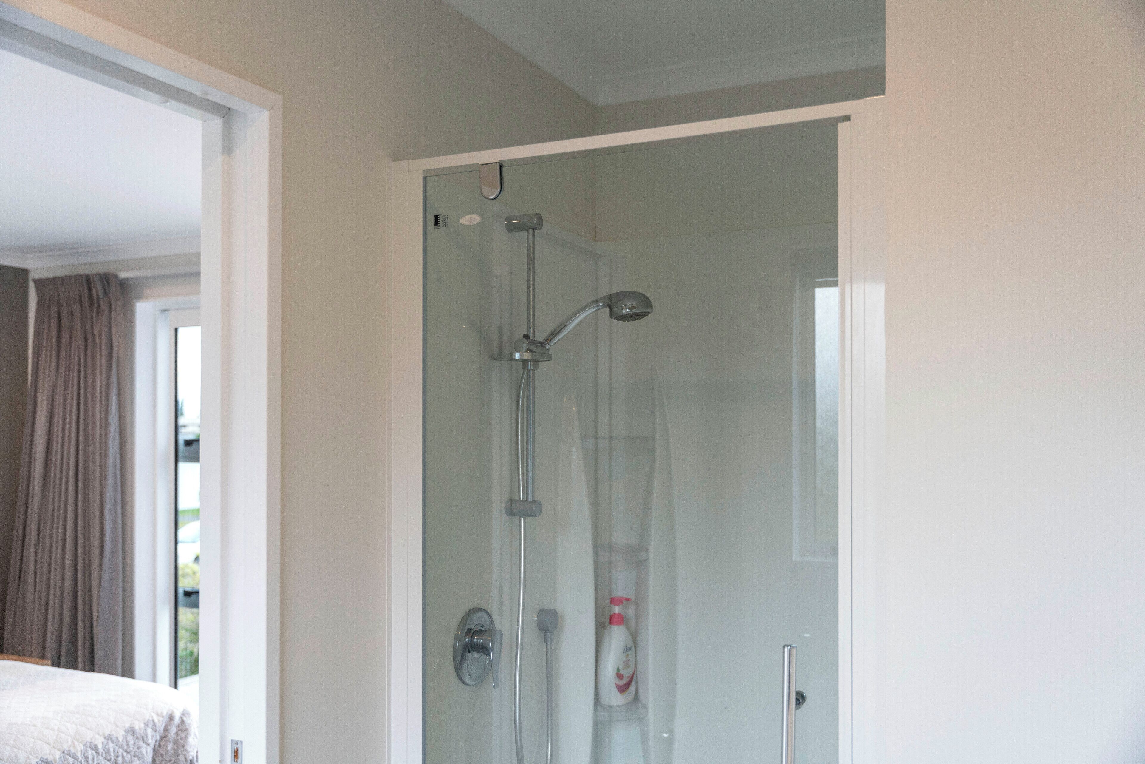 A glass-enclosed shower with a handheld showerhead and a wall-mounted faucet.