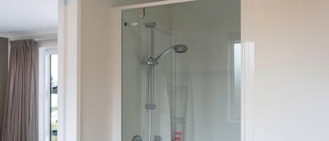 A glass-enclosed shower with a handheld showerhead and a wall-mounted faucet.
