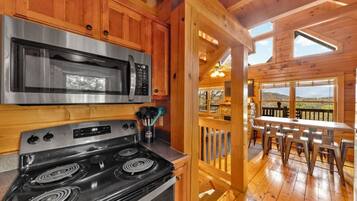 A kitchen with a stainless steel microwave and stove, wooden cabinets, and a view of the outdoor deck with a table and chairs.