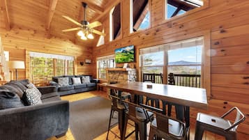 A wooden cabin interior with a sofa, dining table, chairs, and a fireplace.