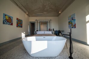A modern bedroom with a large freestanding bathtub, a bed with white linens, and two paintings on the walls. - Stunning Sea-View Historic Home in the Heart of Acireale (Acireale)