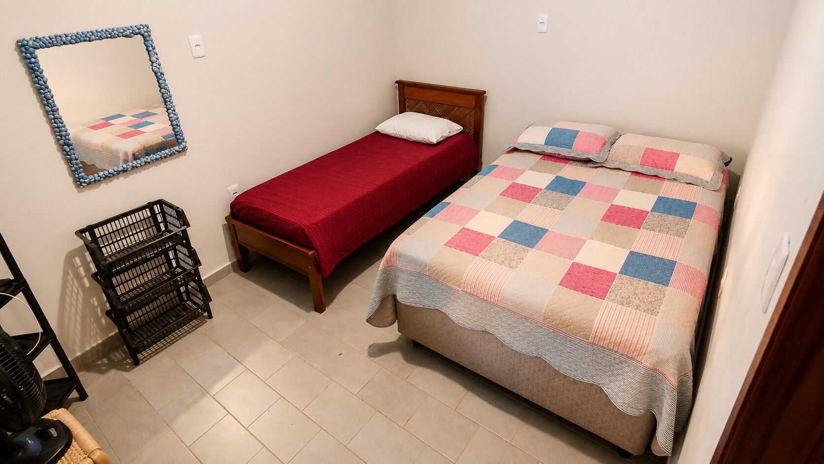 A bedroom with two single beds, a mirror, a black storage unit, and a tiled floor.