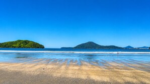 A beach with clear blue water, sandy shore, and distant green hills.