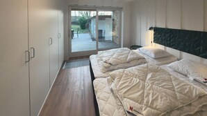Une chambre avec deux lits, un banc en bois, une porte-fenêtre coulissante donnant sur un espace extérieur et une tête de lit moderne.