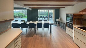 Une cuisine moderne avec un plancher en bois, un coin repas avec des chaises noires et une grande fenêtre donnant sur un jardin.