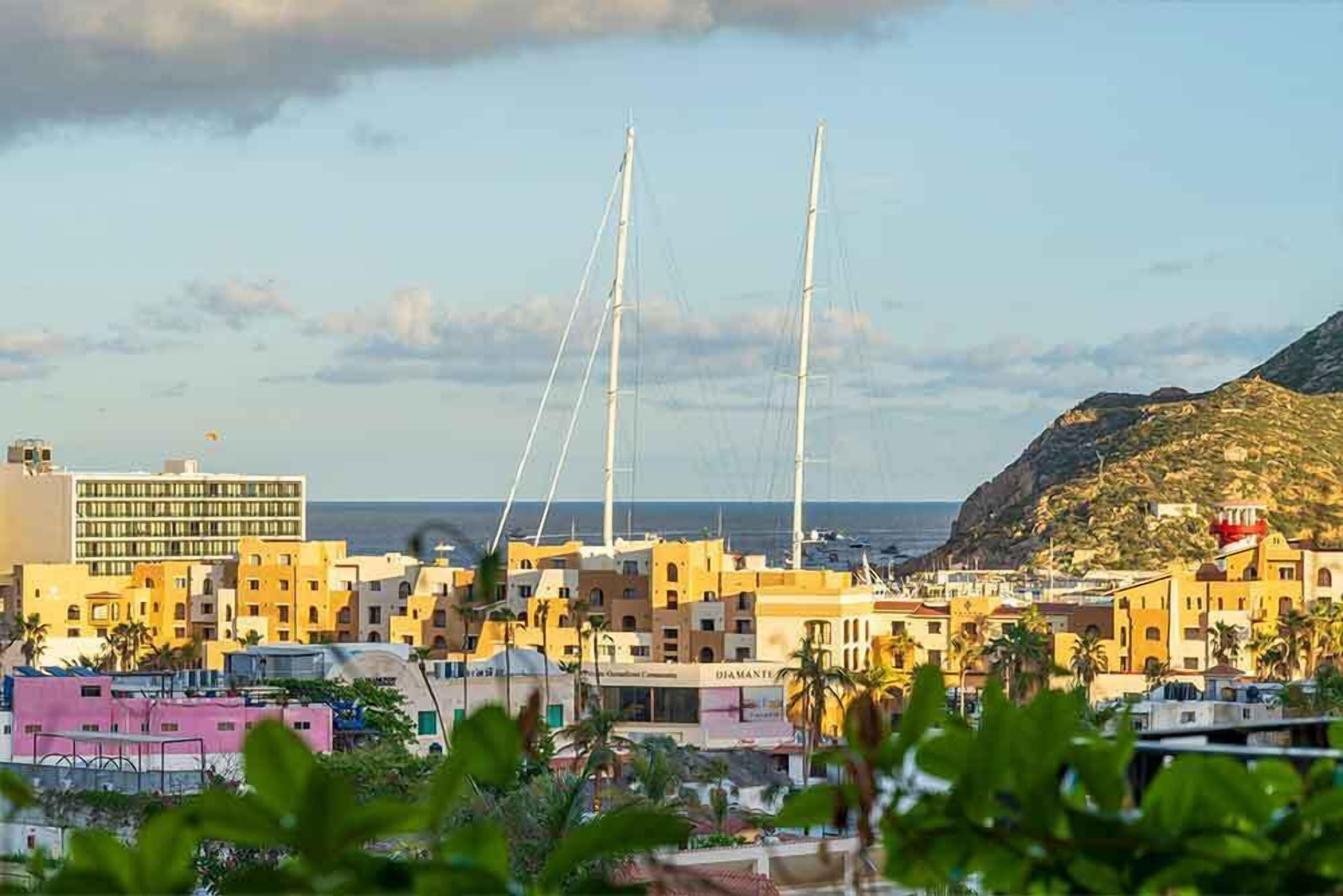 A coastal cityscape with buildings, a prominent hotel with a sign, and a mountain in the background.