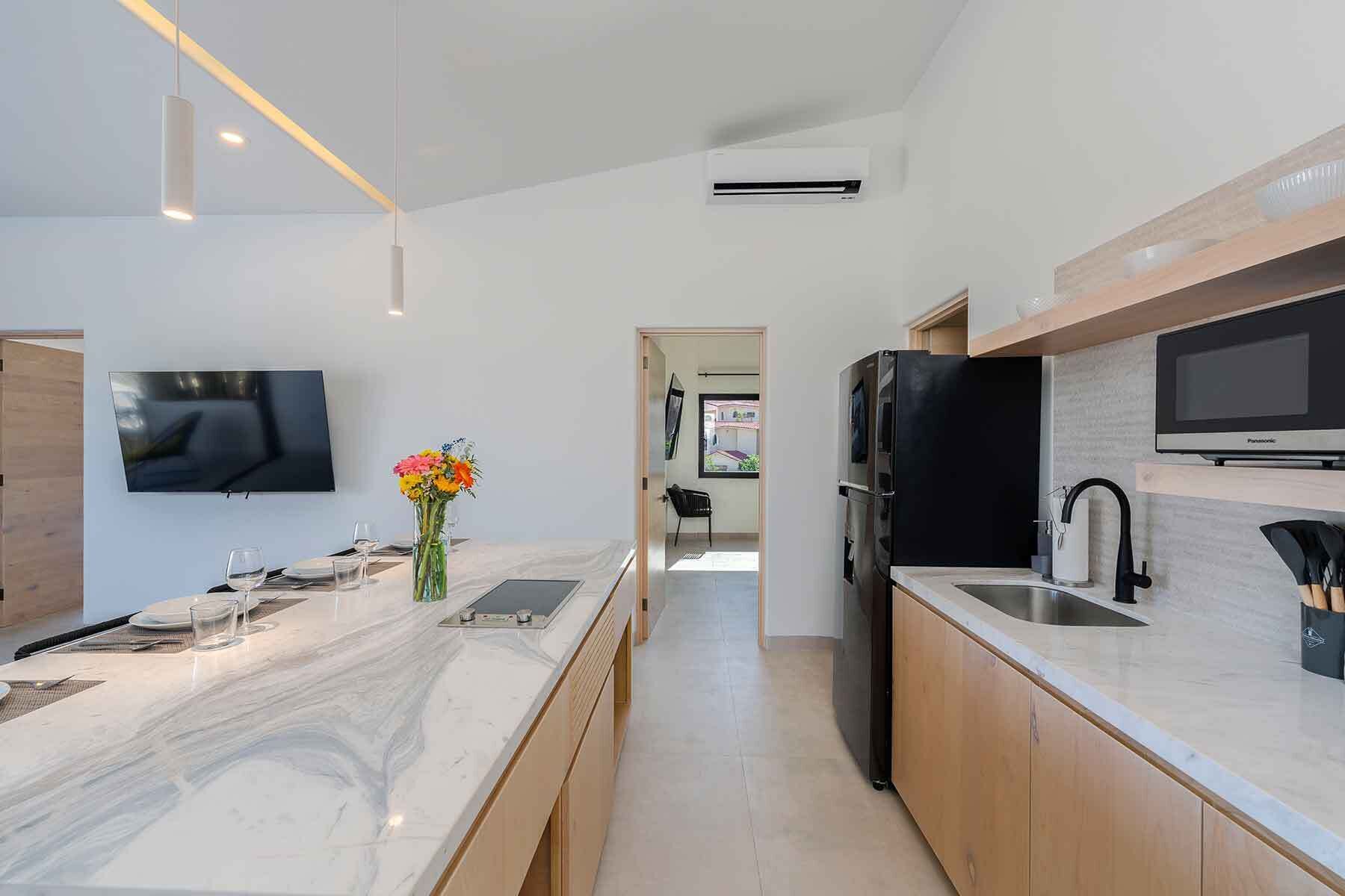 A modern kitchen with a marble countertop, a built-in oven, a sink, and a flat-screen TV.