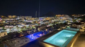En pool på taget med udsigt over bybilledet om natten, inklusive bygninger og et bjerg i baggrunden.