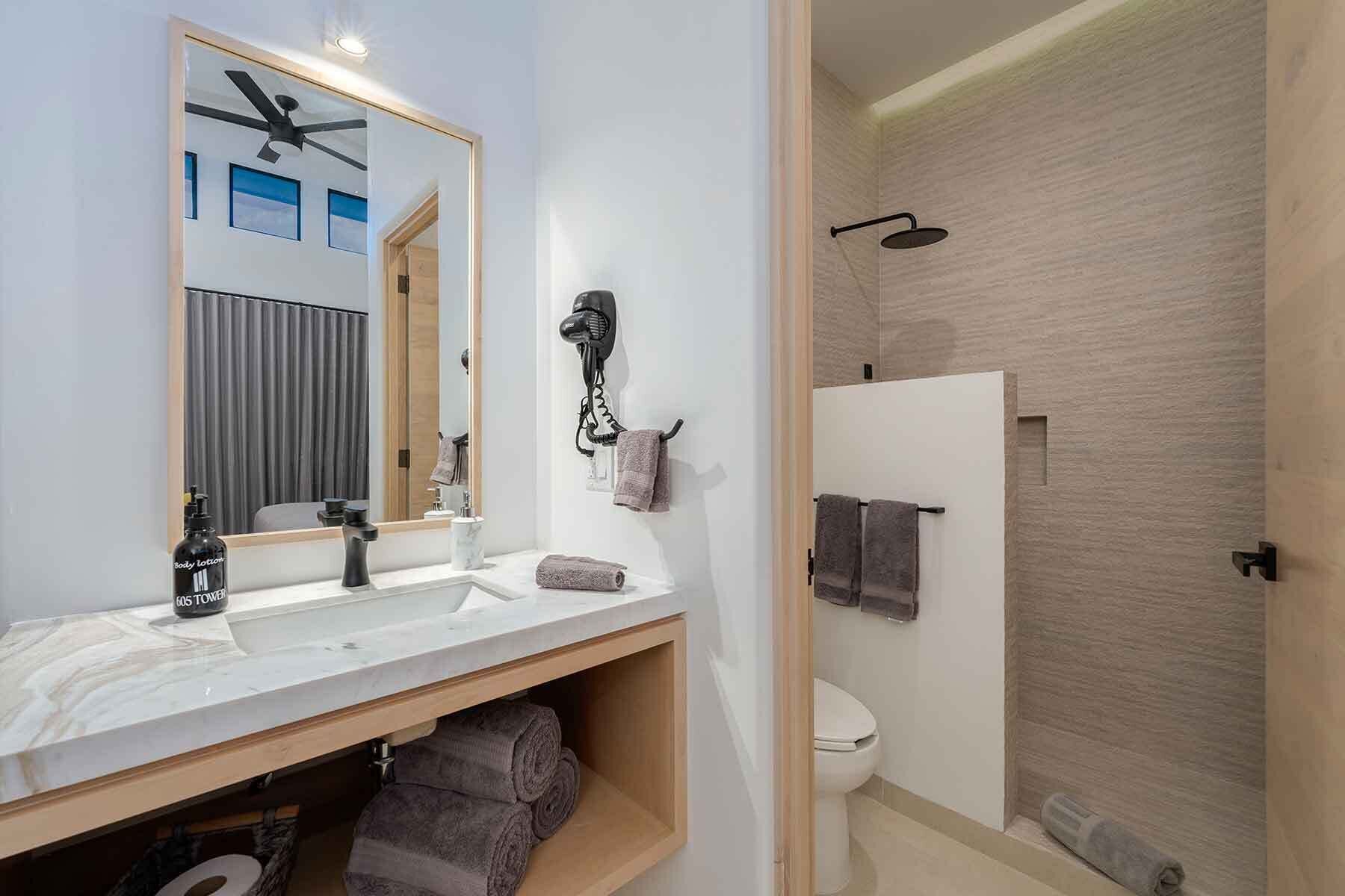 A modern bathroom with a large mirror, two sinks, a hairdryer, and a shower.