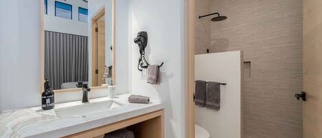 A modern bathroom with a large mirror, two sinks, a hairdryer, and a shower.