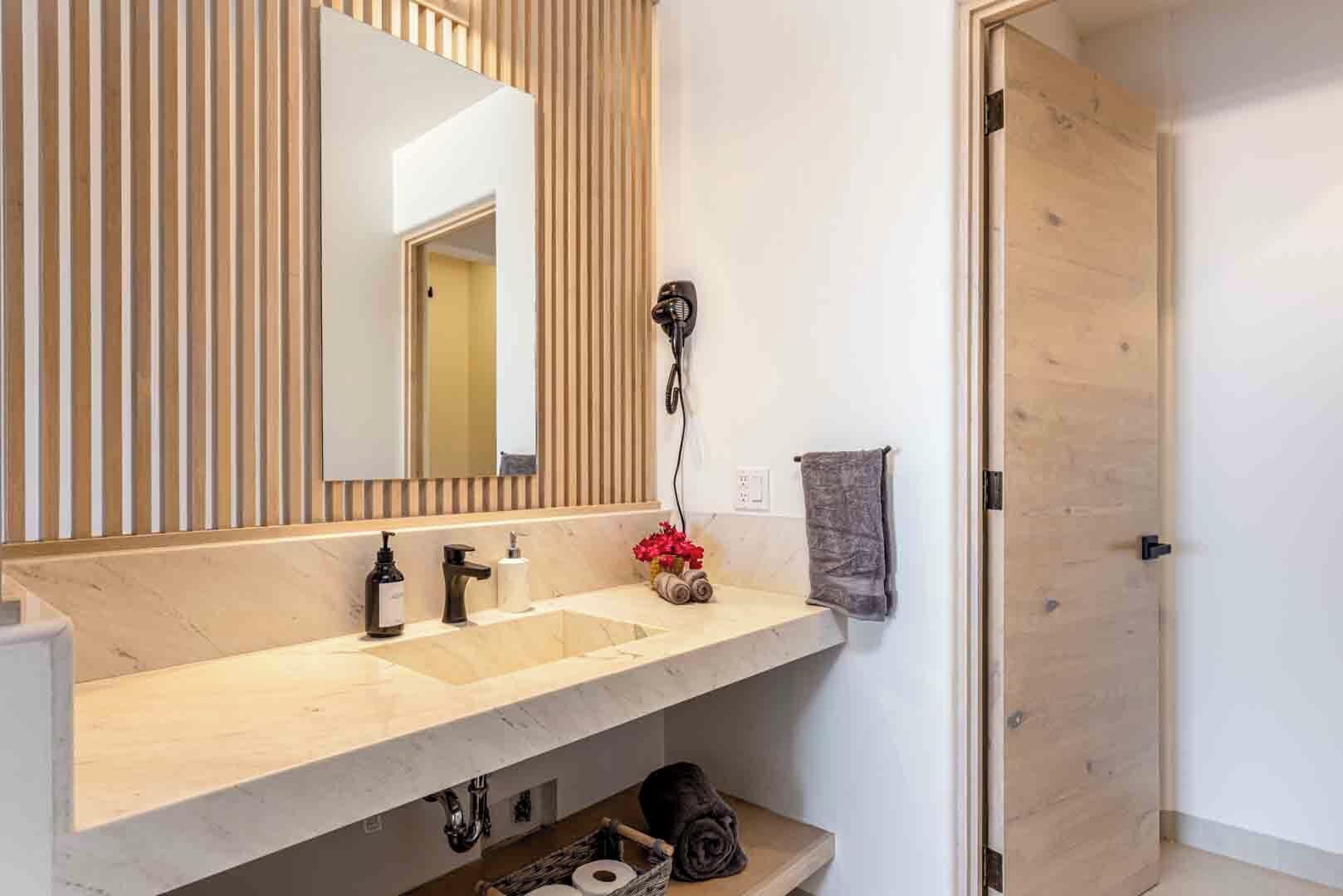 Ein Badezimmer mit Holzlattenwand, einem Waschbecken inklusive Spiegel, einem Fön und einem Handtuchhalter.