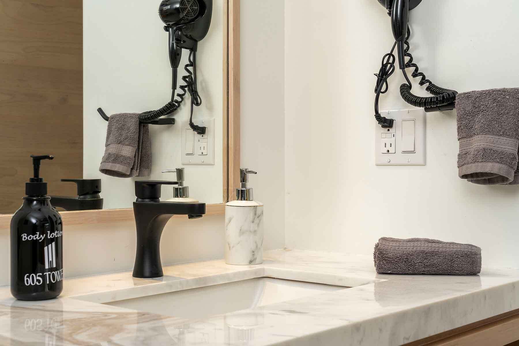 Une salle de bain avec un lavabo en marbre, des distributeurs de savon noirs et blancs, un sèche-cheveux noir et une serviette posée sur le comptoir.