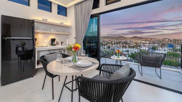 Et moderne køkken med køleskab, spisebord og stole. Der er en balkon med udsigt over bybilledet.