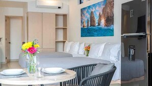 Et moderne hotelværelse med spiseplads, en seng med gråt sengegærde, et maleri af klipper, et køleskab og en kaffemaskine.