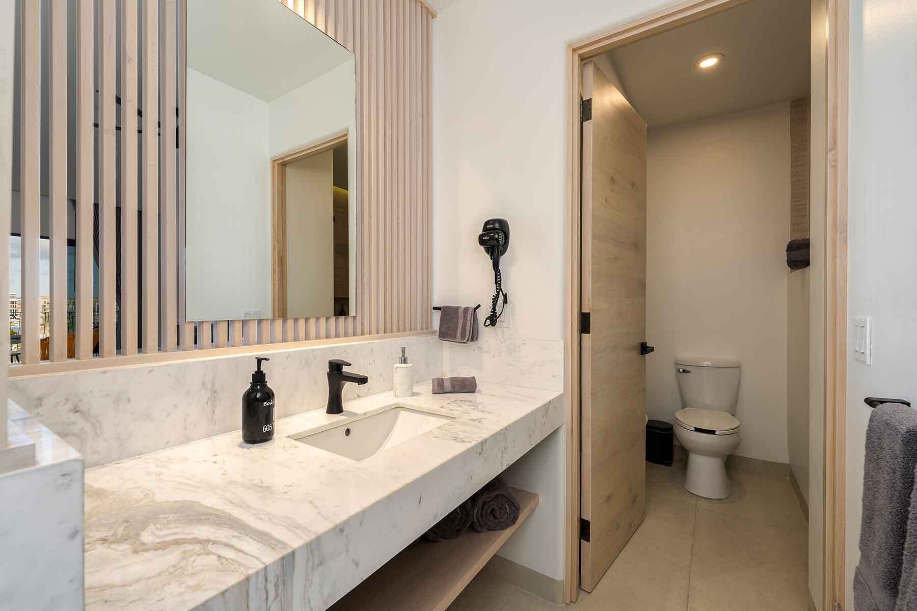 Uma casa de banho moderna com lavatório de mármore, secador de cabelo e sanita.