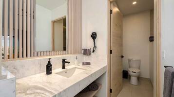 Uma casa de banho moderna com lavatório de mármore, secador de cabelo e sanita.