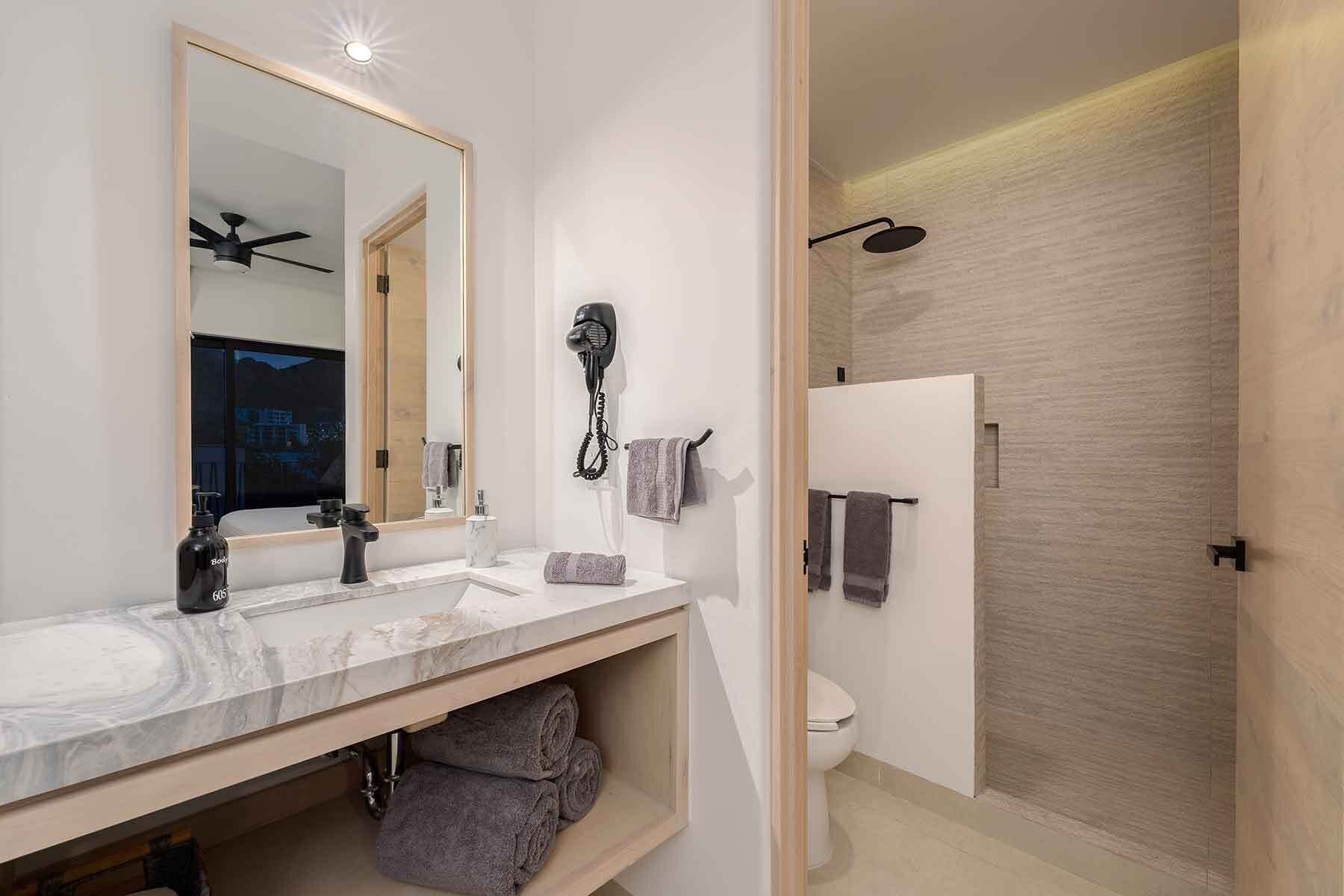 Ein modernes Badezimmer mit Marmorwaschtisch, Fön und Dusche mit Holzverkleidung.