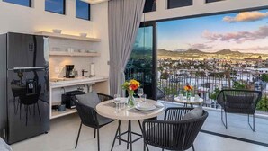 Et moderne køkken med køleskab, spisebord og stole. Der er en balkon med udsigt over bybilledet.