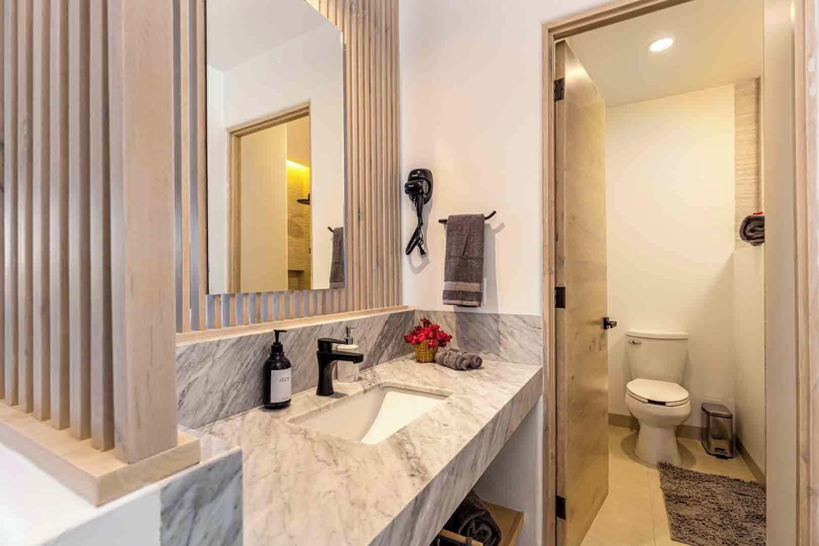 A modern bathroom with a marble sink, a large mirror, and a toilet.