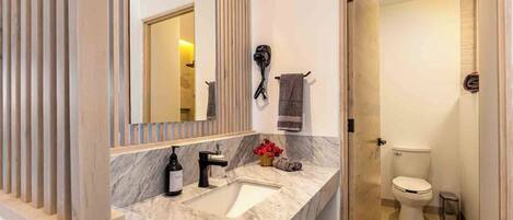A modern bathroom with a marble sink, a large mirror, and a toilet.