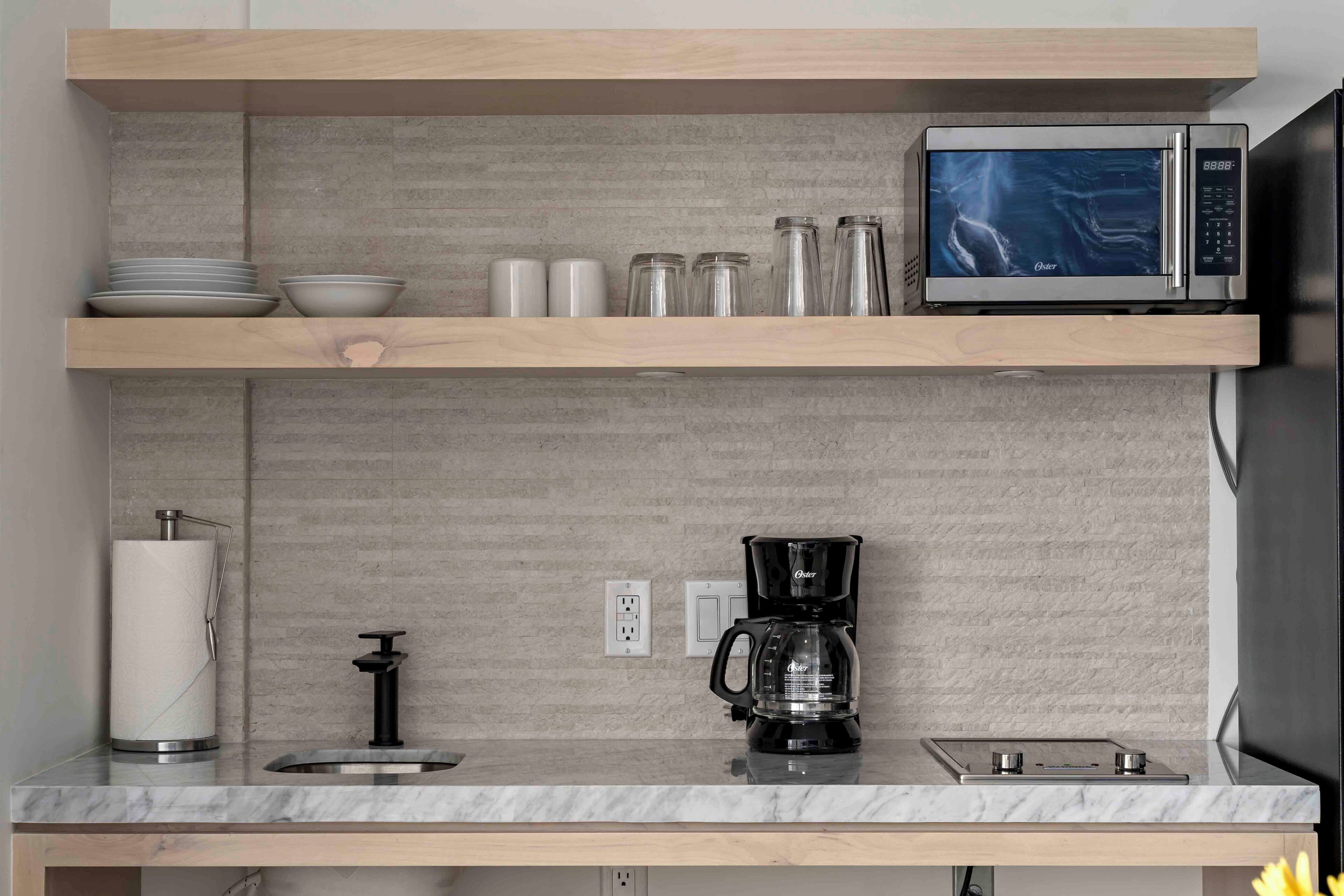 A kitchen with a microwave, coffee maker, and shelves with dishes and jars.