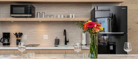 A modern kitchen with a built-in microwave, refrigerator, and coffee maker. There is a dining table set with plates, glasses, and cutlery.