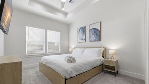 Un dormitorio con una cama de madera, ropa de cama blanca, dos mesitas de noche con lámparas y una obra de arte en la pared.