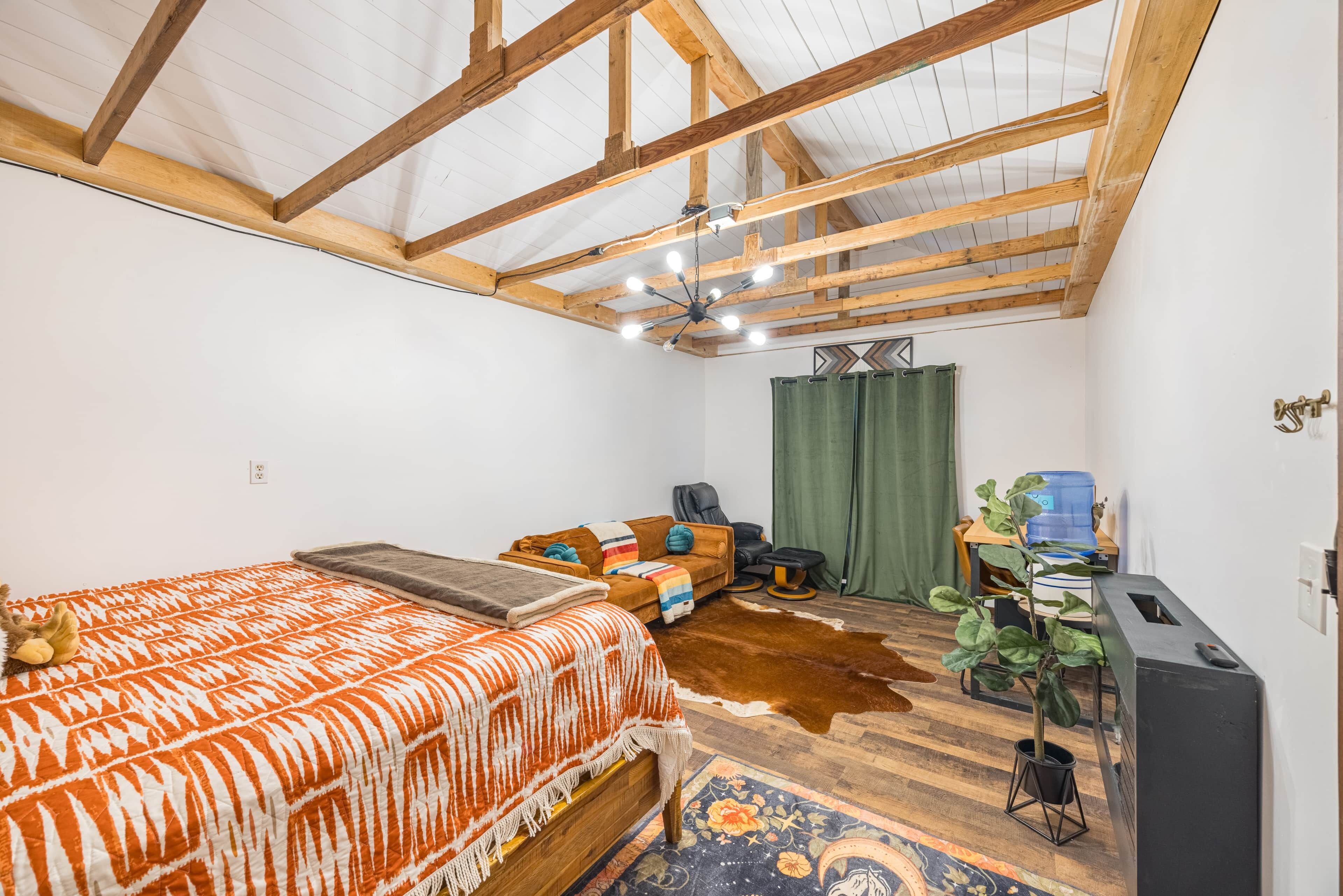 A bedroom with a bed, a sofa, a massage chair, a water dispenser, and a plant.