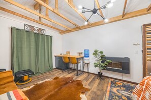 A room with a wooden ceiling, a green curtain, a cowhide rug, a sofa, a coffee table, a water dispenser, and a wall-mounted TV.