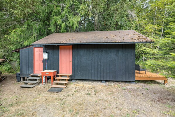 A small cabin with a red door, a wooden deck, and a metal water heater outside.