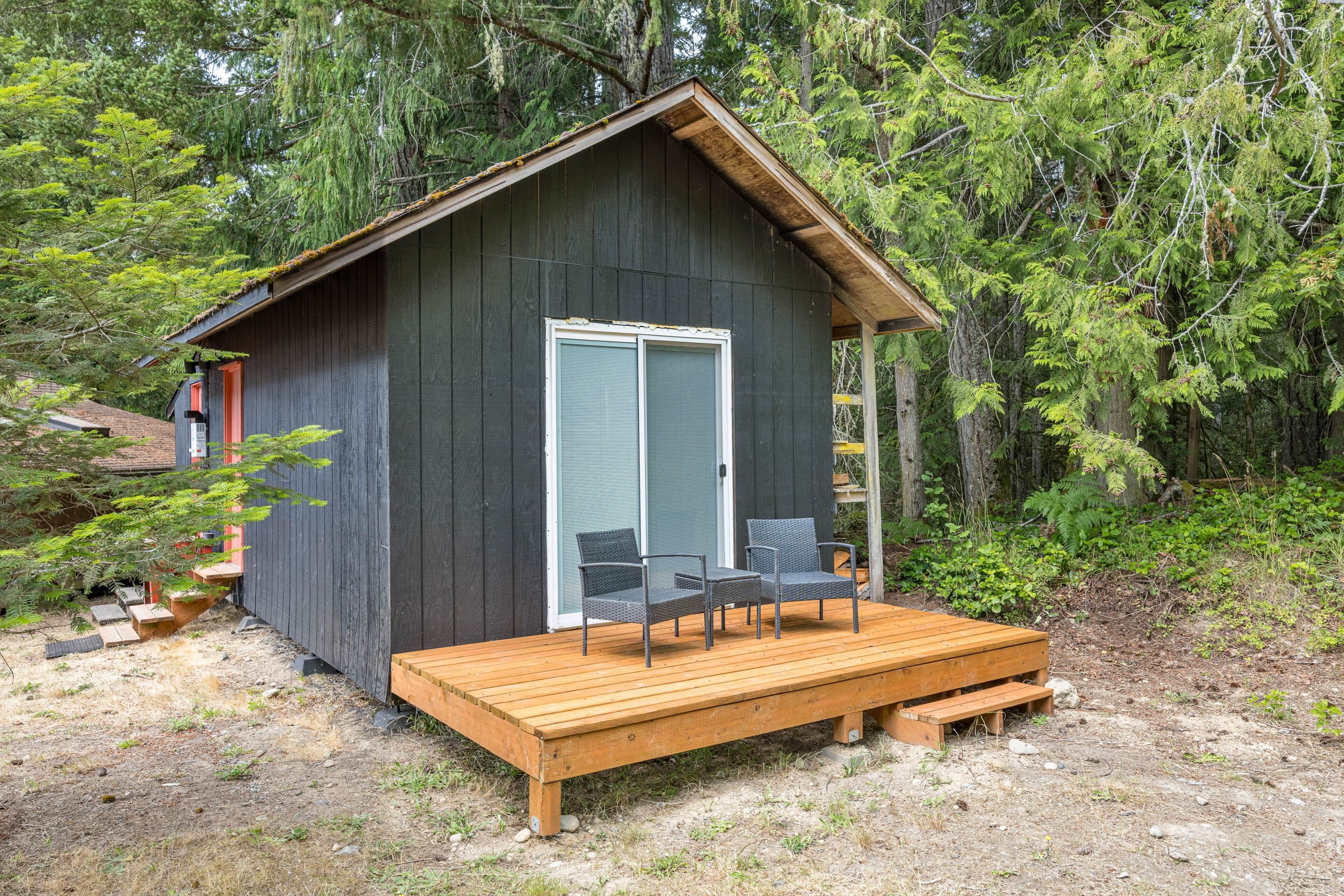 Une petite cabane avec une terrasse en bois, deux chaises et une porte.
