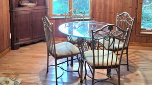A wooden-paneled dining room with a glass table and metal chairs, a wooden cabinet with decorative items, and large windows with a view of greenery. - Lake Eustis Waterfront Sunset House 3/2 Amazing Views! Boat Dock Available!  (Eustis)