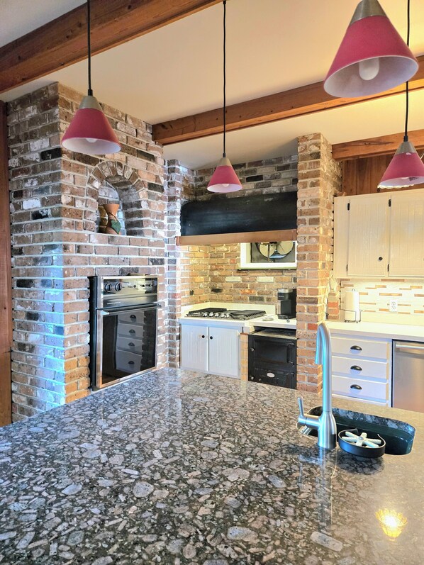 Una cocina con pared de ladrillo, horno empotrado, pileta y lámparas colgantes.