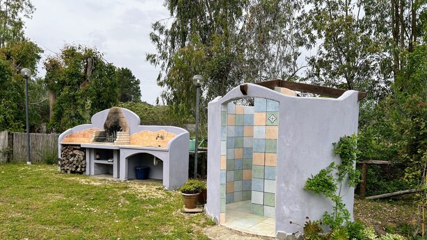 A modern outdoor kitchen with a pizza oven, a built-in seating area, and a small shower enclosure. - DOMO on NEULACHE Country villa consisting of two apts. 5 minutes from the sea (Sardegna)