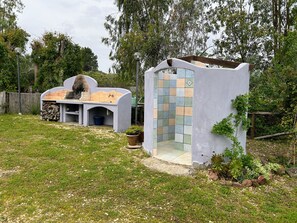 A modern outdoor kitchen with a pizza oven, a built-in seating area, and a small shower enclosure. - DOMO in NEULACHE: A country villa consisting of two apartments. 5 minutes from the ocean (Sardegna)