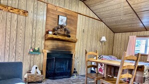 A cozy room with a fireplace, wooden walls, a dining table with chairs, and a sofa. - Mountain cabin with river views Sleeps 4. 15 minutes from Wolf Creek Ski Area. (South Fork)