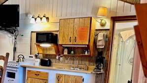 A compact kitchen with wooden cabinets, a microwave, a coffee maker, and a sink. There is a sofa in the foreground and a door leading to another room. - Mountain cabin with river views Sleeps 4. 15 minutes from Wolf Creek Ski Area. (South Fork)