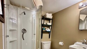 Un baño con ducha de vidrio, inodoro, lavabo y repisa con toallas.