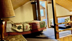 Kodikas ullakkohuone, jossa on yksi sänky, lamppu ja ikkuna.